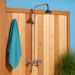 Outdoor shower with a turquoise towel hanging on a wooden panel against a blue sky.